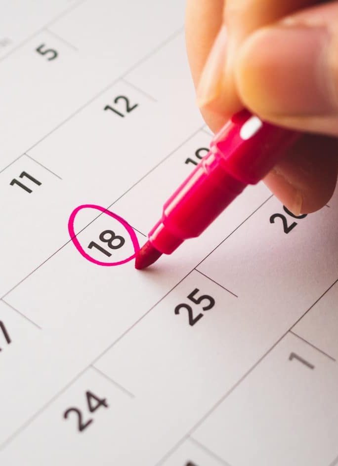 Main d'une personne sur un calendrier, entourant la date du 18 avec un marqueur rose.