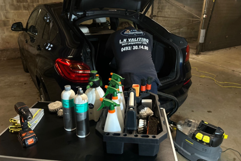 lavage de voiture a domicile Person inspectant le coffre d'une voiture avec des produits de nettoyage à proximité.