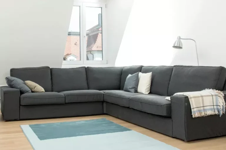 lavage canapé 5 places et plus Canapé d'angle gris avec coussins, plaid, et tapis sur un sol en bois clair.